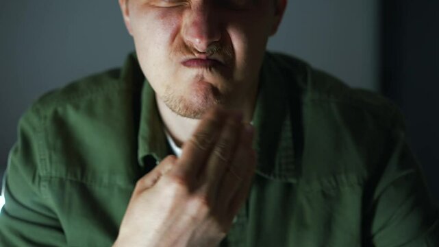 A guy in a dark room puts his fingers in his mouth to trigger a gag reflex.
The man feels sick and burps.
Food poisoning and nausea in a man.
Fingers in mouth