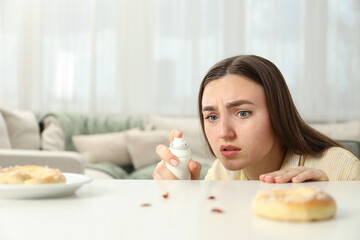Plakat Emotional young woman spraying insecticide onto cockroaches at white table indoors. Pest problem