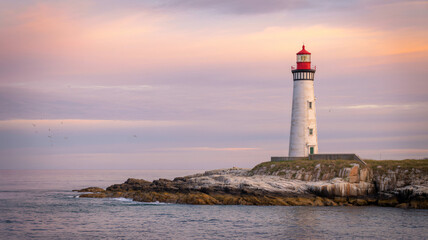 White lighthouse with a red top on a rocky coast under a pastel sky