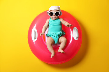 Cute little baby in sunglasses with inflatable ring on yellow background