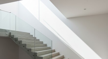 Obraz premium Minimalist concrete staircase with clear glass railing and bright natural light streaming from a skylight onto a pristine white wall, creating strong diagonal shadows.