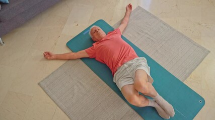 Video of Elderly man practicing spinal twist exercise on a yoga mat at home,flexibility and mobility
