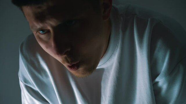 Asthma and difficulty breathing in a young man in a dark room.
European man is breathing heavily due to fatigue and severe stress.
Physical activity and breathing problems