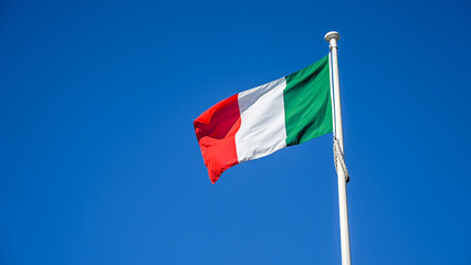 Italian flag on the pole. Green, white and red colors of the Italian flag. Flag of Italy against blue sky. 
