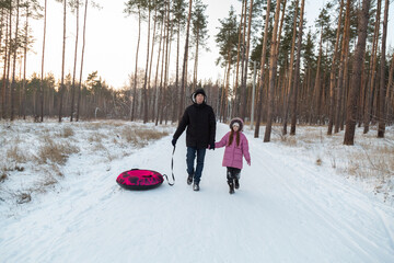 Dad with his daughter walking with snow tubing in the winter forest