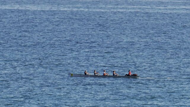 Distant view of a rowing team of four people practicing on calm water, with a coxswain seated at the front