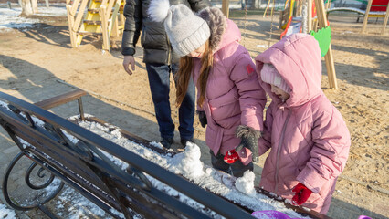 Grandfather with granddaughters making a little snowman in sunny winter day