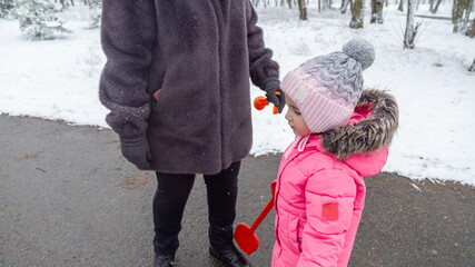 Grandmother with little girl granddaughter on snowy weather outdoors.