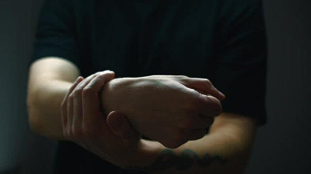 A man in a black T-shirt massages his sore hand.
Arm pain and intense massage.
Physiotherapy of the hand after injury.
Hand pinched.
Bruised and sprained arm