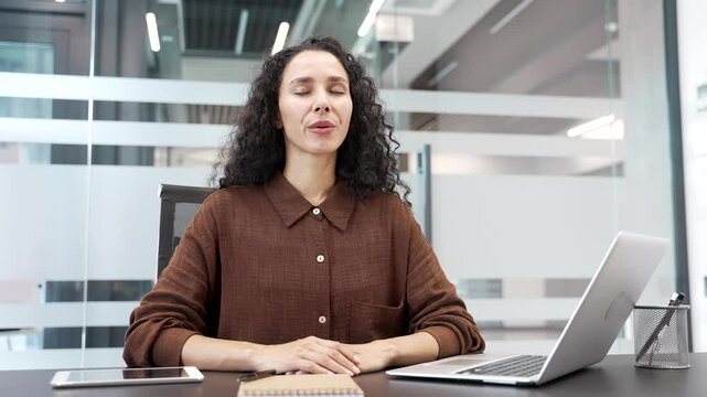Young businesswoman relaxing breathing deeply while sitting at a desk at a workplace in a business office. Calm happy female employee resting with her eyes closed. Joyful woman took a break from work