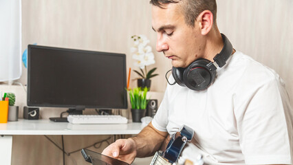 A young man with a smartphone while holding an electric guitar at home.