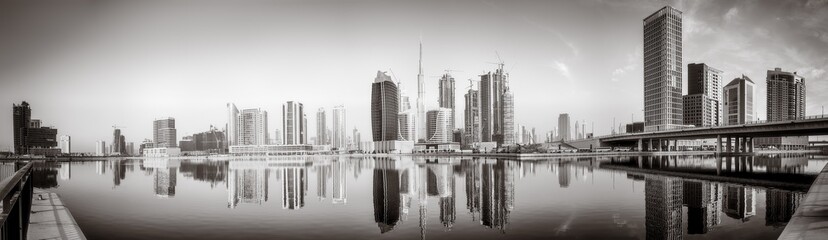 Fototapeta premium Monochrome city skyline with tall skyscrapers reflecting on calm water under a cloudy sky, Dubai Marina bay UAE