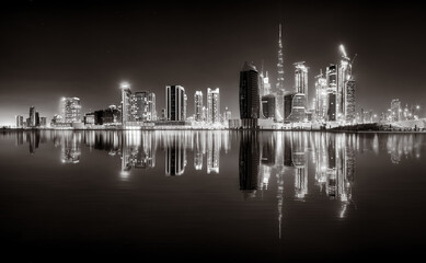 Urban city skyline with illuminated skyscrapers and waterfront railing in black and white at night, Dubai Marina bay UAE