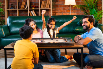 Parents and children playing carrom board game indoors, laughing and aiming striker with focus
