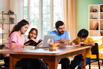 Obraz premium Parents teaching kids at home using laptop and books during study session in living room