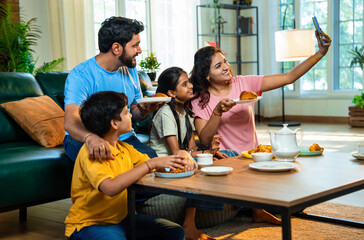Indian family posing for selfie while enjoying samosa and tea time in warm and happy atmosphere
