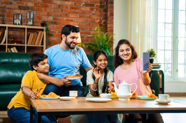 Family making video call during tea time with samosas, smiling and bonding in living room