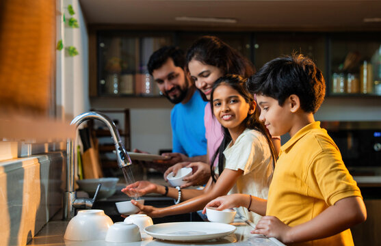 Indian family washing dishes in kitchen sink, cleaning utensils after enjoying dinner together - Powered by Adobe
