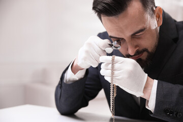 Appraiser evaluating luxury necklace at white table indoors, space for text