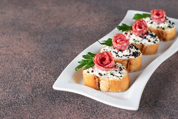 Canapes with cream cheese and sausage on bread toast in white plate