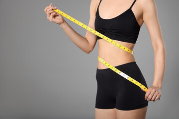 Woman with slim body and measuring tape on gray background, closeup. Space for text