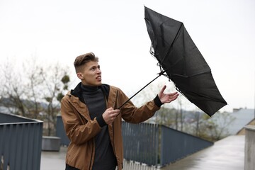 Man with broken umbrella fighting wind under rain outdoors