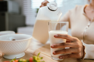 A woman prepares a healthy breakfast in her kitchen, pouring fresh milk into a bowl of muesli with blueberries—nutritious and homemade.