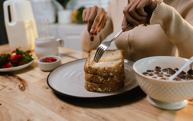 A woman enjoys a peaceful morning, spreading fresh strawberry jam on bread during breakfast—homemade, healthy, and full of natural sweetness.