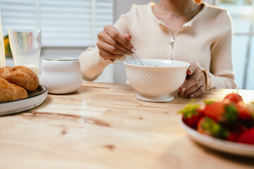 A woman enjoys a peaceful morning, spreading fresh strawberry jam on bread during breakfast—homemade, healthy, and full of natural sweetness.