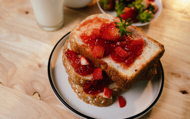 Fresh homemade strawberry jam spread on toasted bread slice, served on plate for a delicious red sweet breakfast snack indoors.