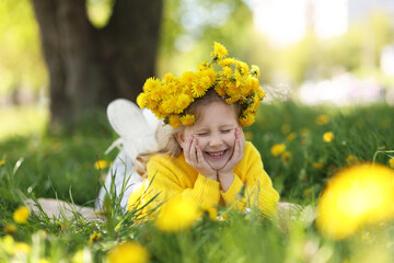 Cute little girl wearing wreath of dandelions on green grass in park