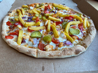 A hearty oven pizza with veggies, meat and fries rests on a paper box in a kid-friendly cafe