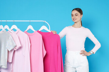 Smiling fashion stylist and rack with clothes on light blue background