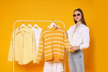 Smiling fashion stylist and rack with clothes on yellow background