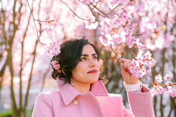 Portrait of a woman in pink coat under cherry blossoms in spring