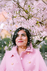Portrait of a woman in pink coat under cherry blossoms in spring