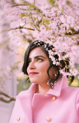Portrait of a woman in pink coat under cherry blossoms in spring