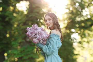Obraz premium Smiling woman with bouquet of lilac flowers outdoors in morning
