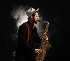 Naklejka premium Professional musician playing saxophone on black background with smoke. Space for text