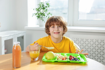 Cute little boy eating lunch at wooden table in school