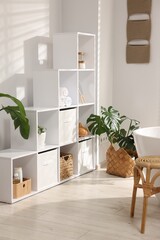 Stylish bathroom with shelving unit, bathtub, table and houseplants