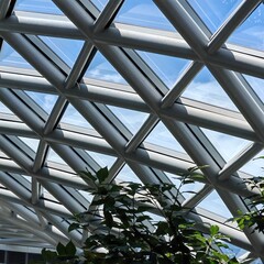 Abstract view of modern glass and steel roof structure with geometric triangular patterns and blue sky background.