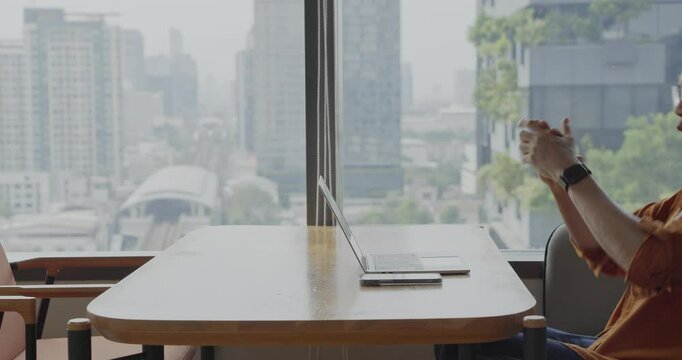 Senior Asian businessman wearing headset celebrates success during online meeting in modern co-working space. Remote work and business communication concept.