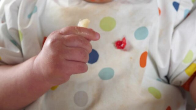 Dirty hands of a baby taking fruit pieces and putting them into his mouth, baby led weaning method