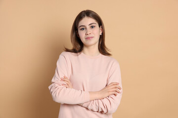 Fototapeta premium Portrait of beautiful teenage girl with crossed arms on beige background