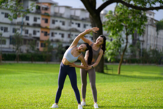 Asian women exercising together outdoors with personal trainer assisting during side bending exercise