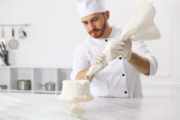 Confectioner decorating cake with cream at white marble table in kitchen, space for text