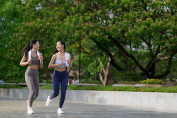 Obraz premium Two female athletes are jogging and chatting during their workout in a park