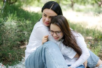 Naklejka premium Young woman embracing with her daughter in the meadow of the park.