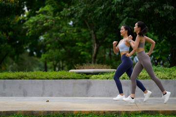 Two female athletes jogging side by side in a lush green park, enjoying their outdoor workout